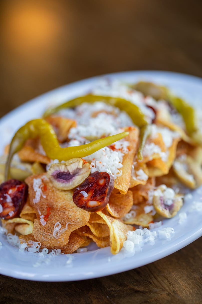 Crispy potato chips topped with chorizo slices, green peppers, and shredded cheese on a white plate.