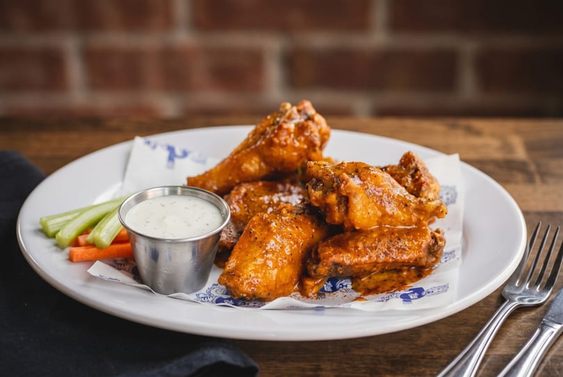 Plate of buffalo wings with ranch dressing, celery, and carrots on a wooden table.