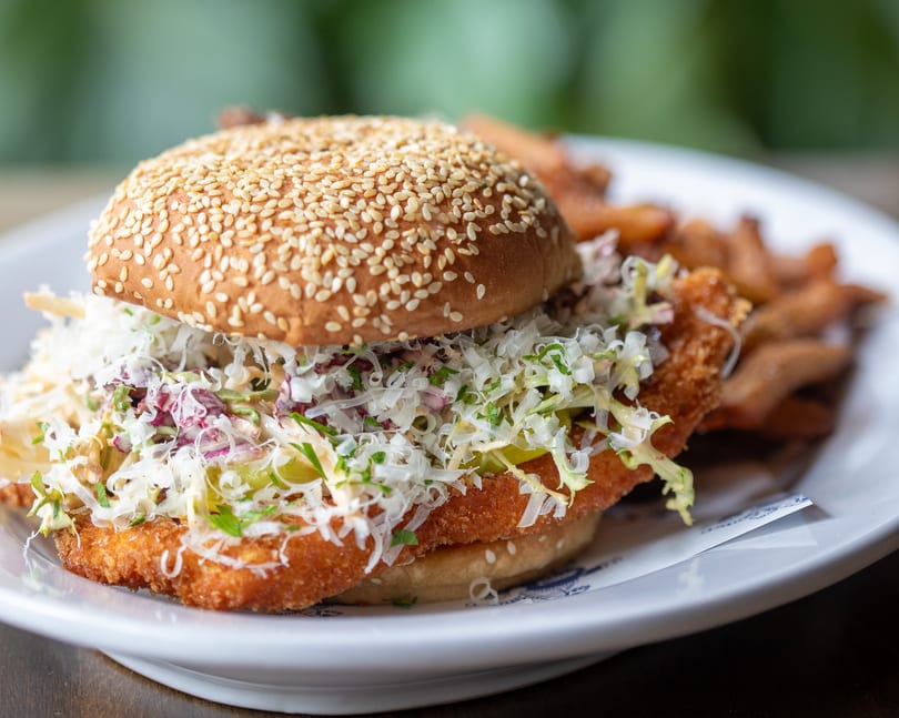Crispy fried chicken sandwich with coleslaw and pickles on a sesame bun, served with fries.