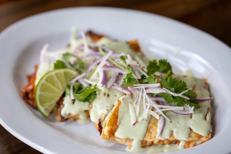 Three quesadillas topped with green sauce, cilantro, red onion, radish, and a lime wedge.