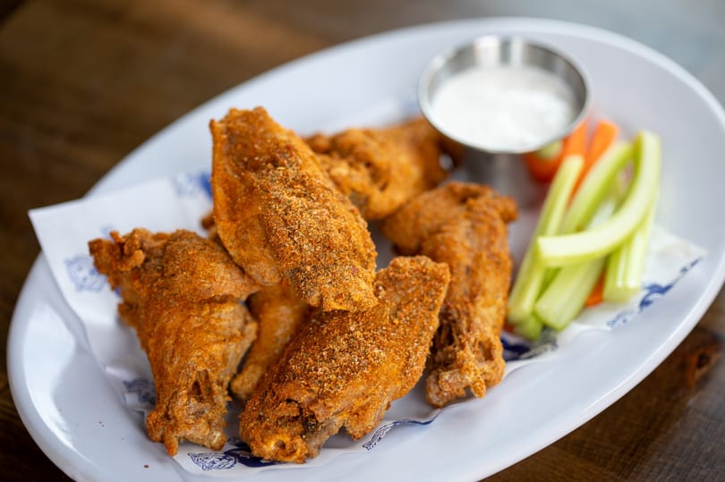 Crispy seasoned chicken wings with celery, carrots, and ranch dip on a white plate.