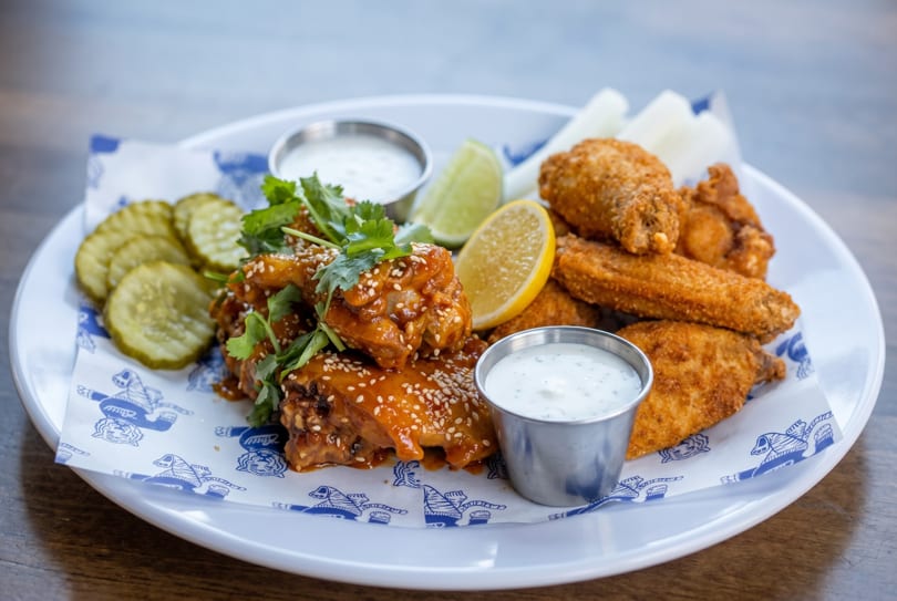 A plate of two kinds of chicken wings, pickles, celery, and dipping sauces.