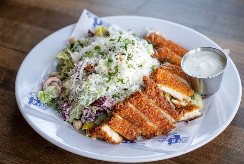 Crispy chicken strips and a fresh salad topped with shredded cheese and herbs, with a side of ranch.